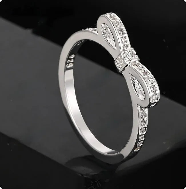 Silver-coloured bow-shaped ring with clear rhinestone embellishments on a white background