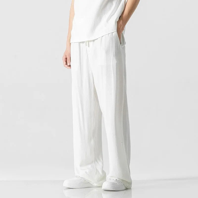 Men's beige loose-fit straight-leg linen trousers with drawstring waist, shown on a model.