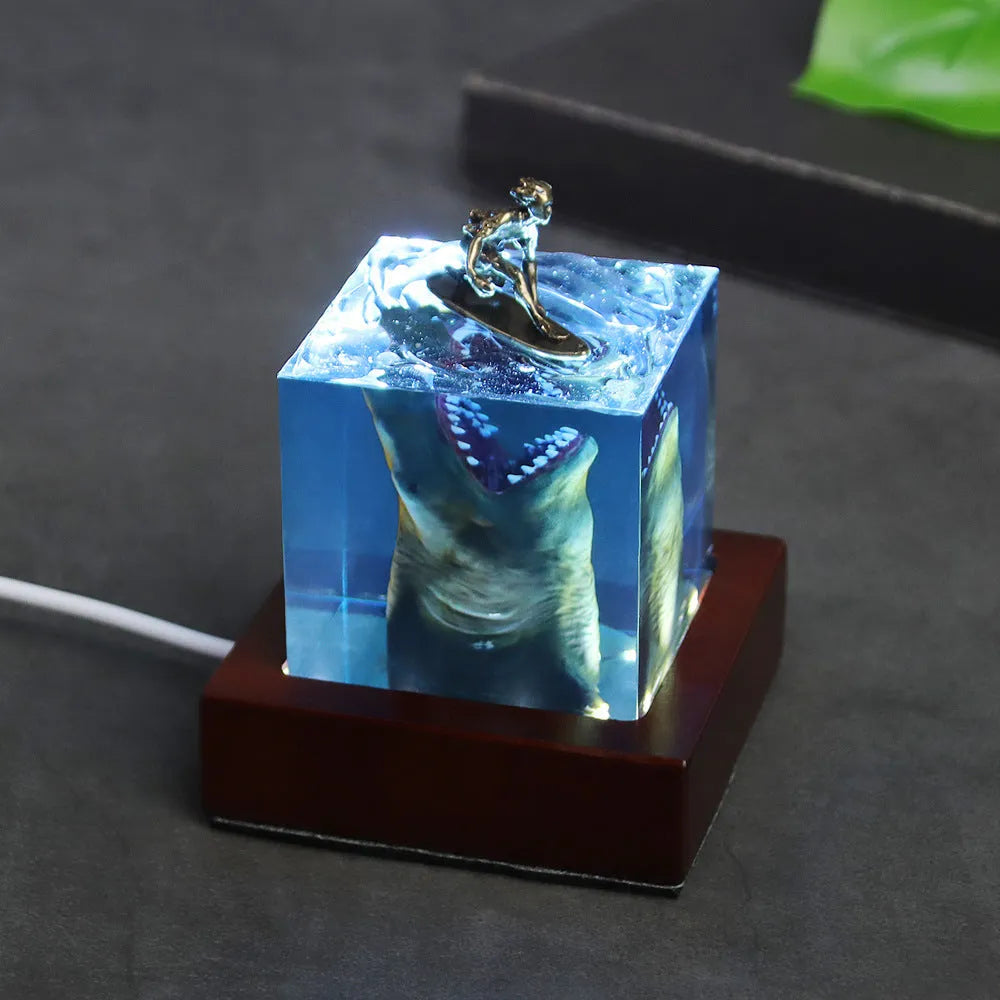 Clear epoxy resin ornament with shark surfing scene inside, on a plastic lamp holder base.