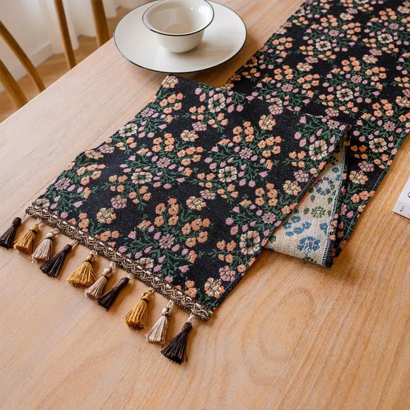 Dark blue striped table runner with jacquard bouquet pattern and tassel ends on a wooden table.