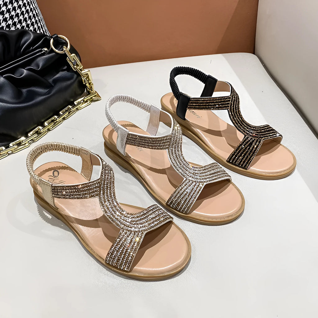Gold women's patent leather sandals with rhinestone detailing and a non-slip sole on a sandy beach.