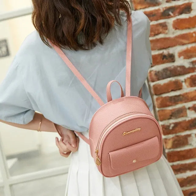 Small black women's PU shoulder backpack worn as backpack, showing zipper closure and compact size