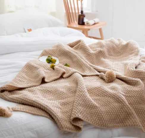 Nordic style fringed knit throw blanket in a neutral colour, shown draped over a sofa.