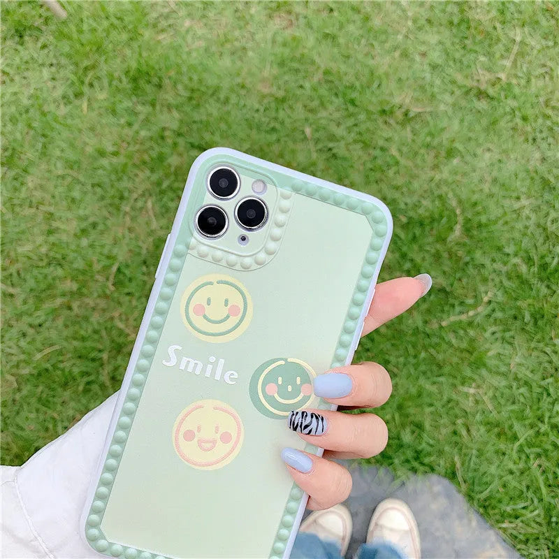 Green TPU iPhone case with a smiley face and polka dot geometric design on a table.
