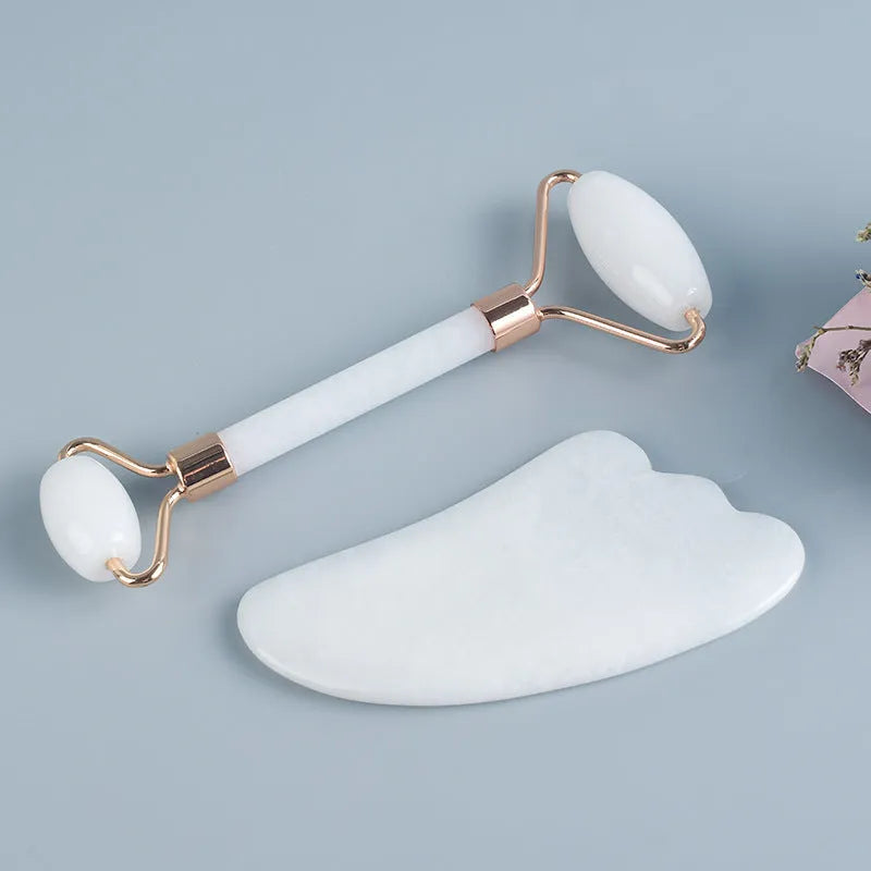 White jade facial roller and gua sha board set on a plain surface.