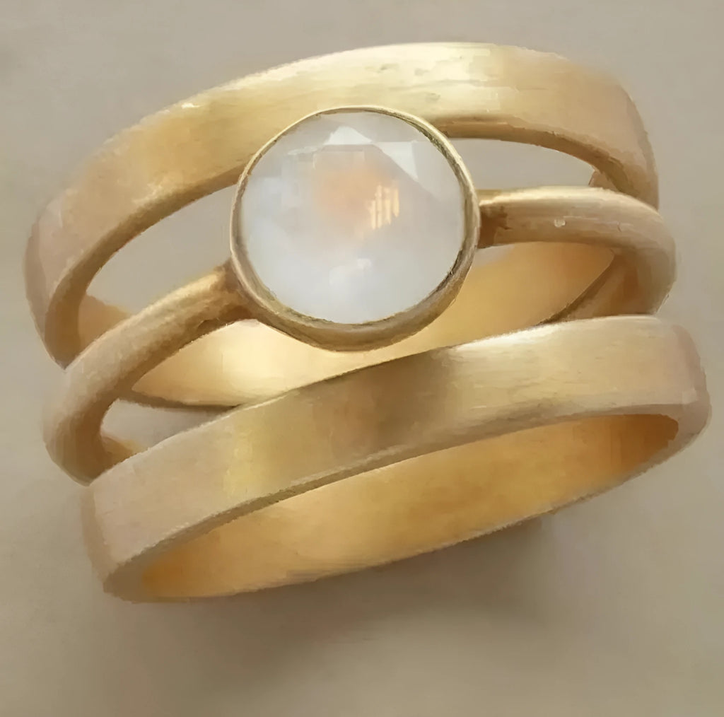 Gold-plated hollow geometric titanium steel ring with micro-inlaid white chalcedony on a grey background.