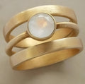 Gold-plated hollow geometric titanium steel ring with micro-inlaid white chalcedony on a grey background.