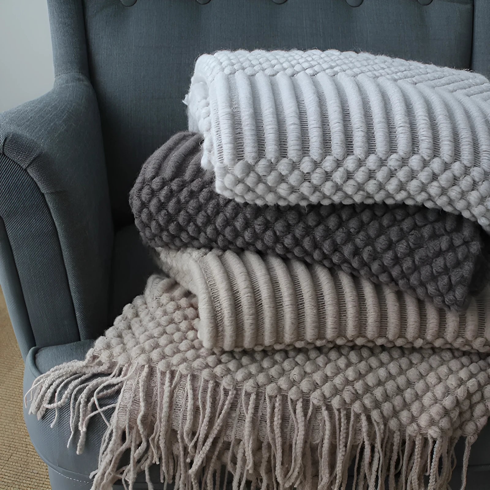 Small light grey polyester nap blanket folded on a sofa, showing its size.
