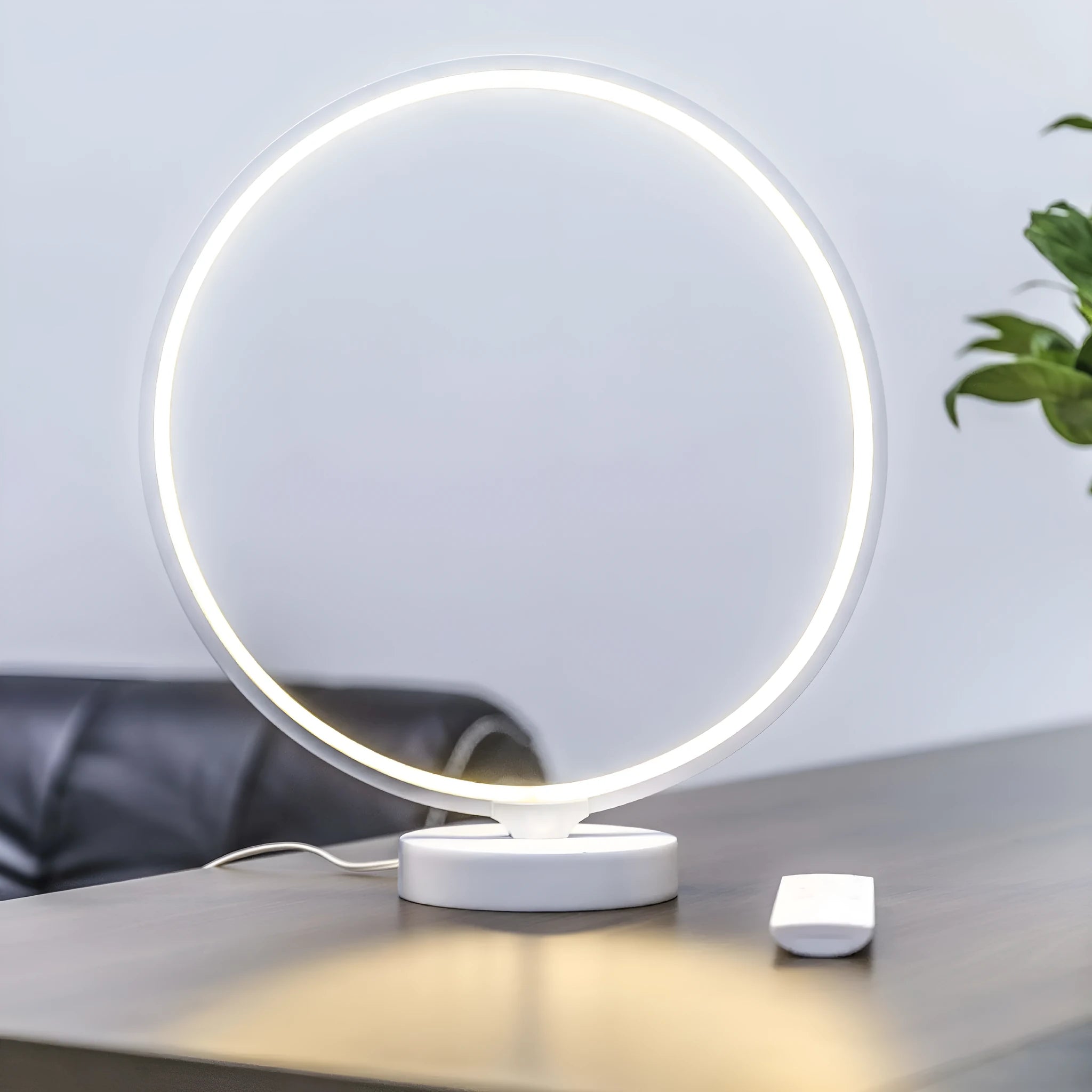 White full moon shaped table lamp with soft glow, placed on a surface with remote control.