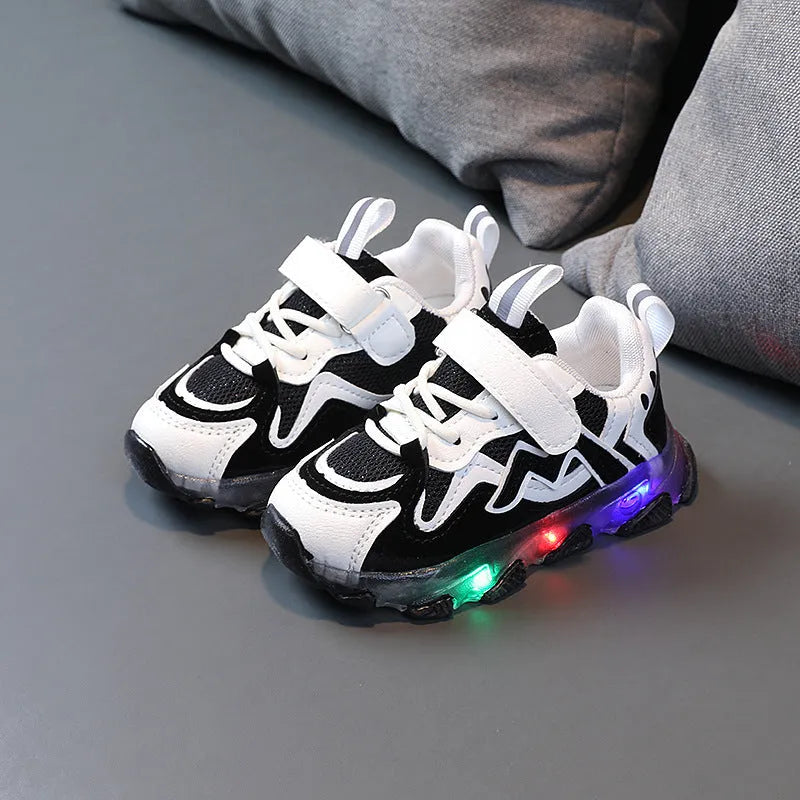 Kids' black mesh sneakers with Velcro strap and light grey rubber sole on a paved surface.