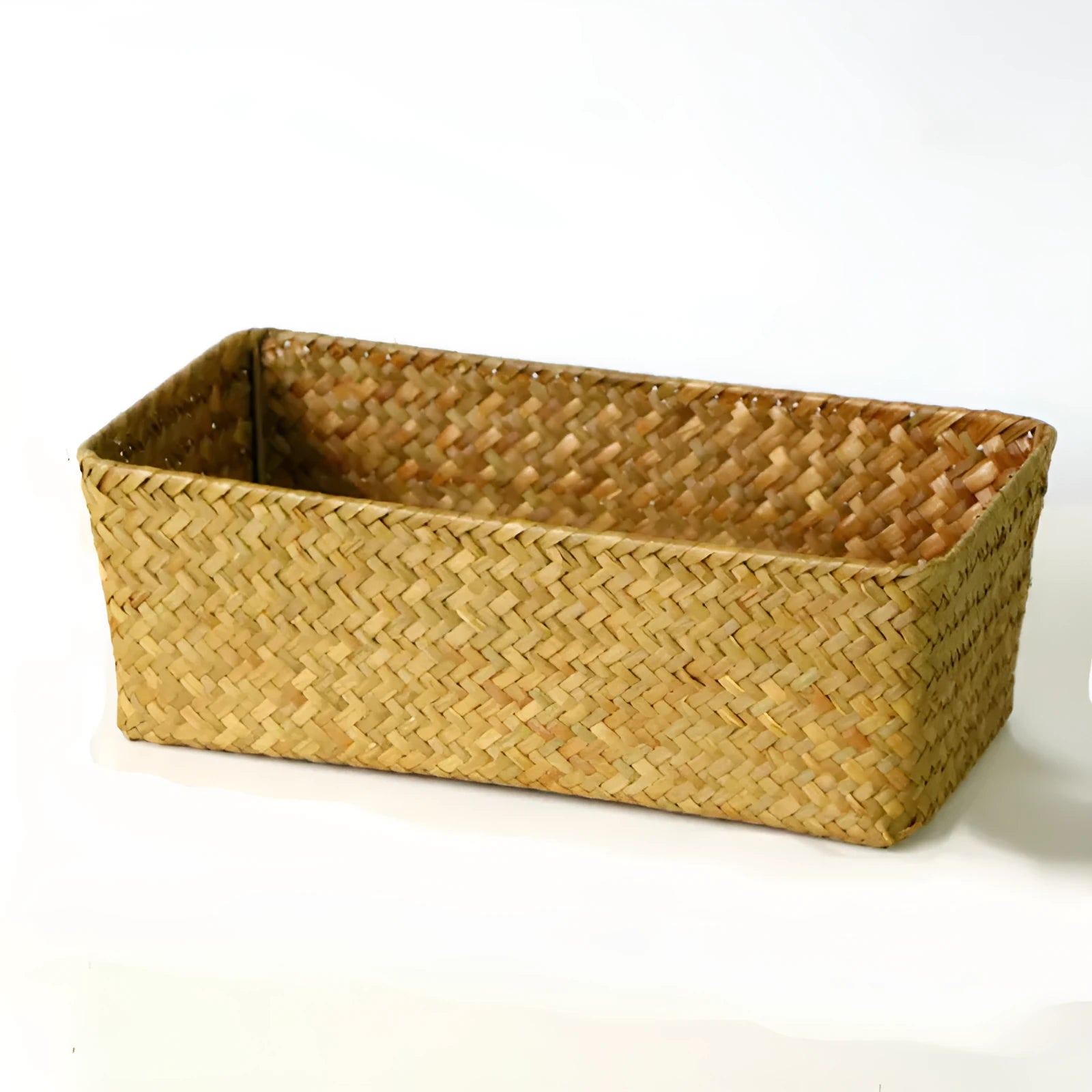 Natural brown woven straw desk storage box holding pens and cosmetic bottles on a wooden table.