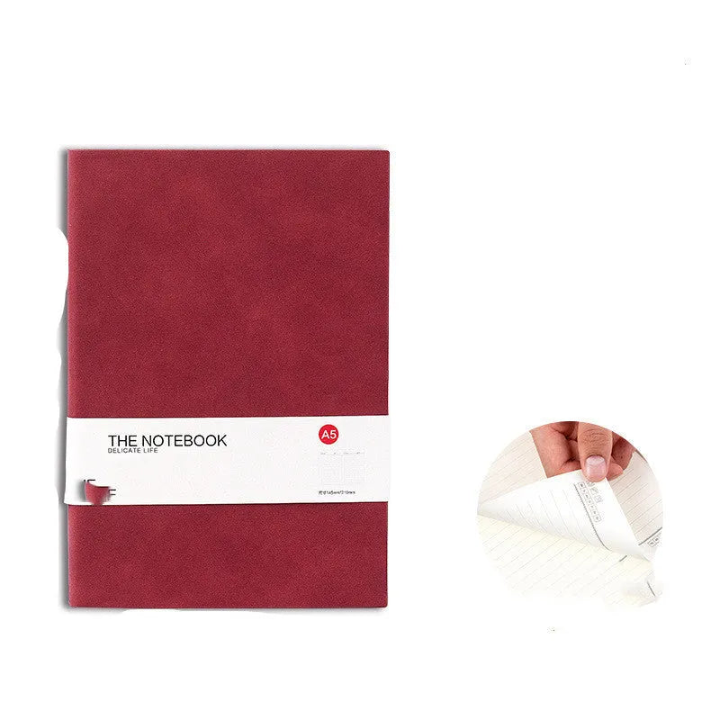 Simple solid colour thickened A5 notebook in green, open on a desk with a pen.