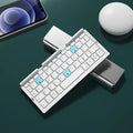 Silver folding Bluetooth keyboard open with tablet on stand, showing compact size and 60-key layout