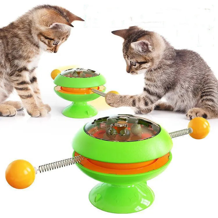 Rotating turntable cat toy with colourful base and transparent top containing three catnip balls, on a wooden floor.