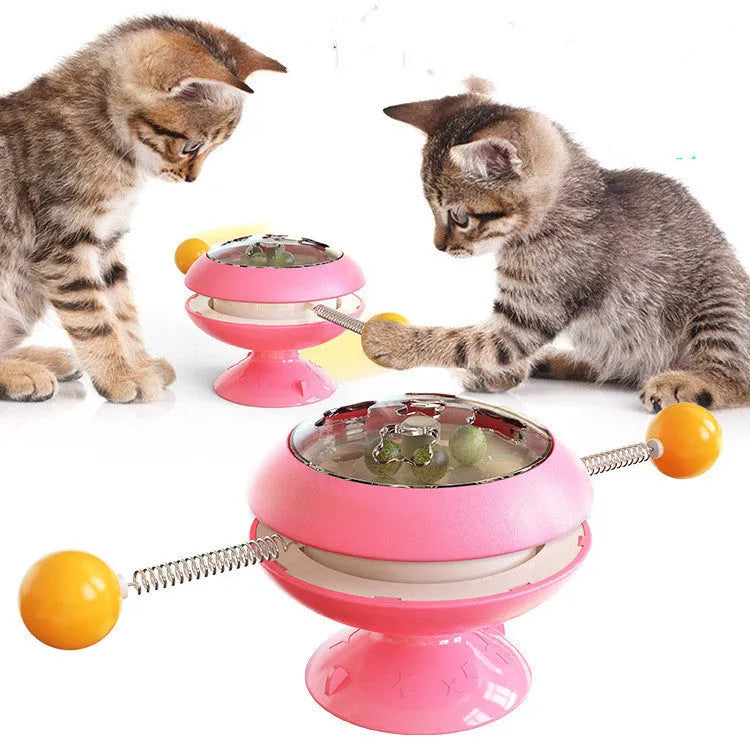 Rotating turntable cat toy with colourful base and transparent top containing three catnip balls, on a wooden floor.