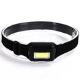 Compact black outdoor LED headlight with adjustable polyester strap on a grey background.