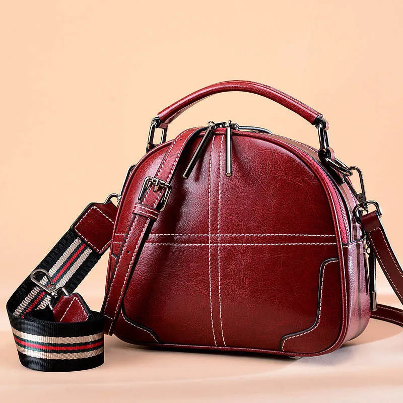 Round wine red leather women's handbag with zipper and double soft handles on a neutral background.