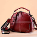 Round wine red leather women's handbag with zipper and double soft handles on a neutral background.
