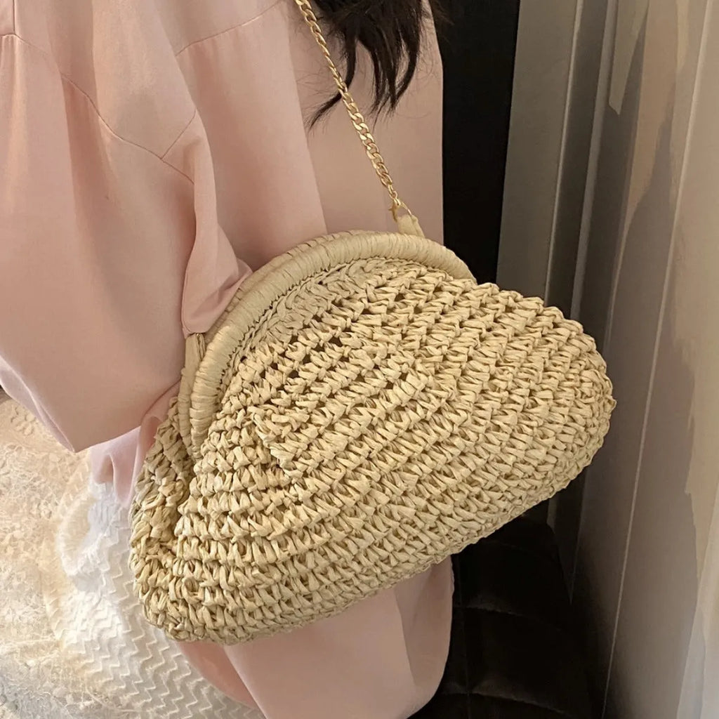 Women's khaki straw shoulder bag with chain detail and shell shape on a neutral background
