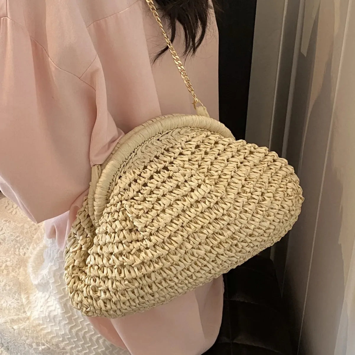 Women's khaki straw shoulder bag with chain detail and shell shape on a neutral background