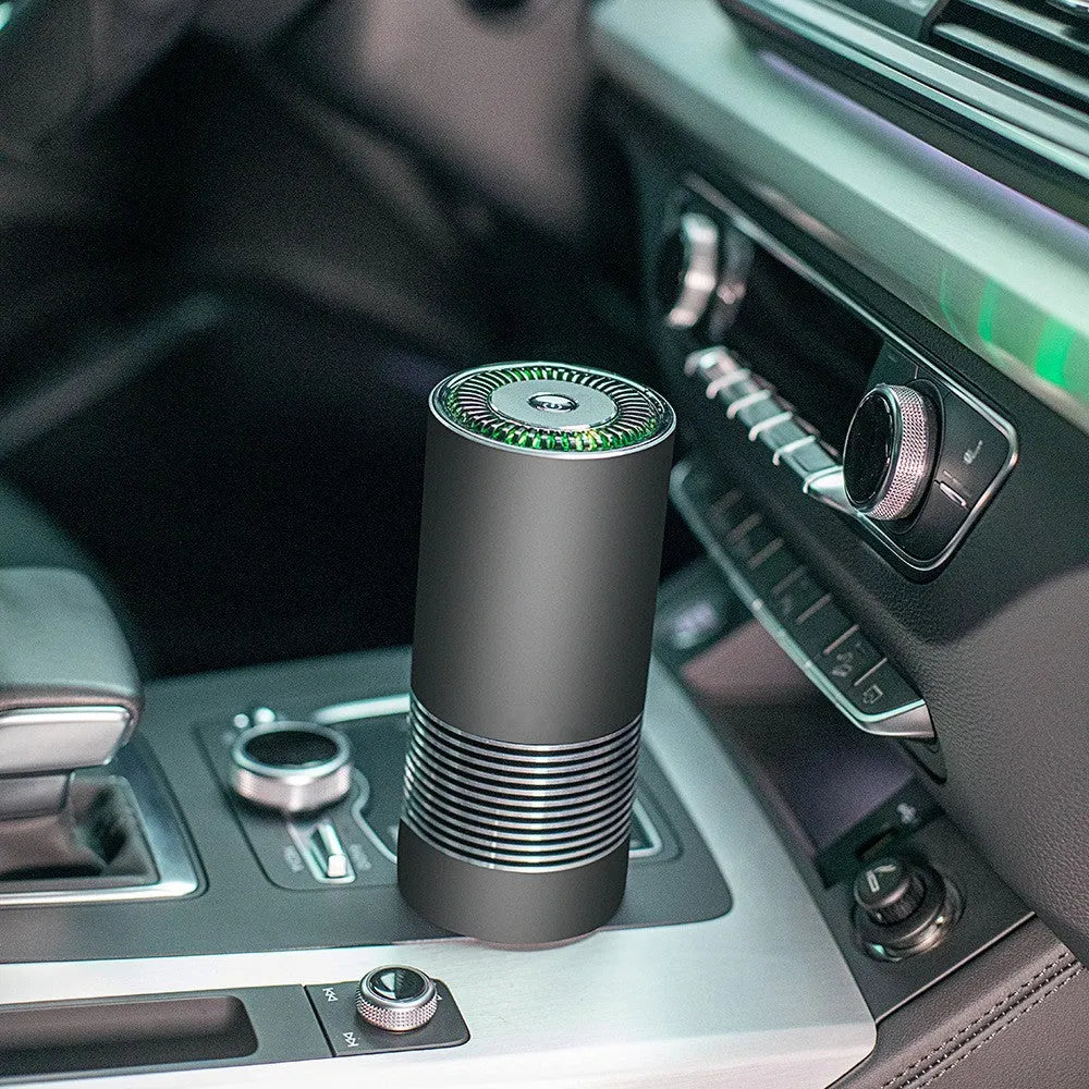 Compact cylindrical car air purifier in metallic grey with USB cable, shown next to a car vent for scale.