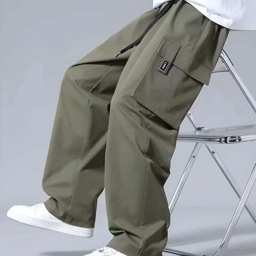 Boy wearing army green straight leg cargo pants with large pockets and a drawstring waist.