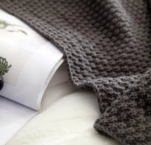 Nordic style fringed knit throw blanket in a neutral colour, shown draped over a sofa.