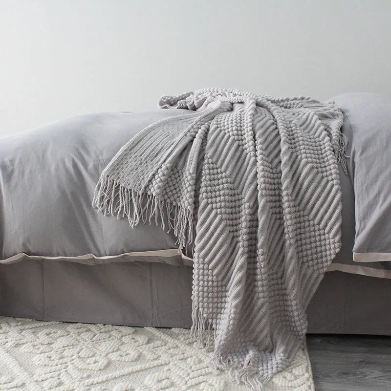 Small light grey polyester nap blanket folded on a sofa, showing its size.