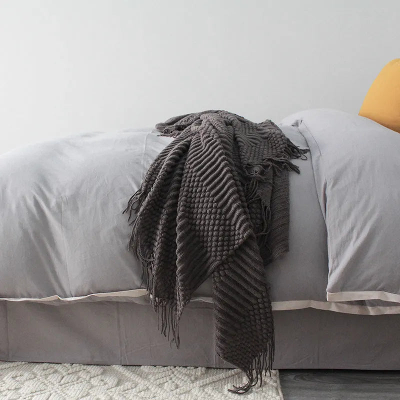 Small light grey polyester nap blanket folded on a sofa, showing its size.