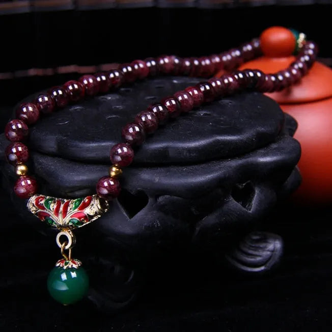 Close-up of a natural red garnet bead bracelet with a golden toad charm on a wrist.