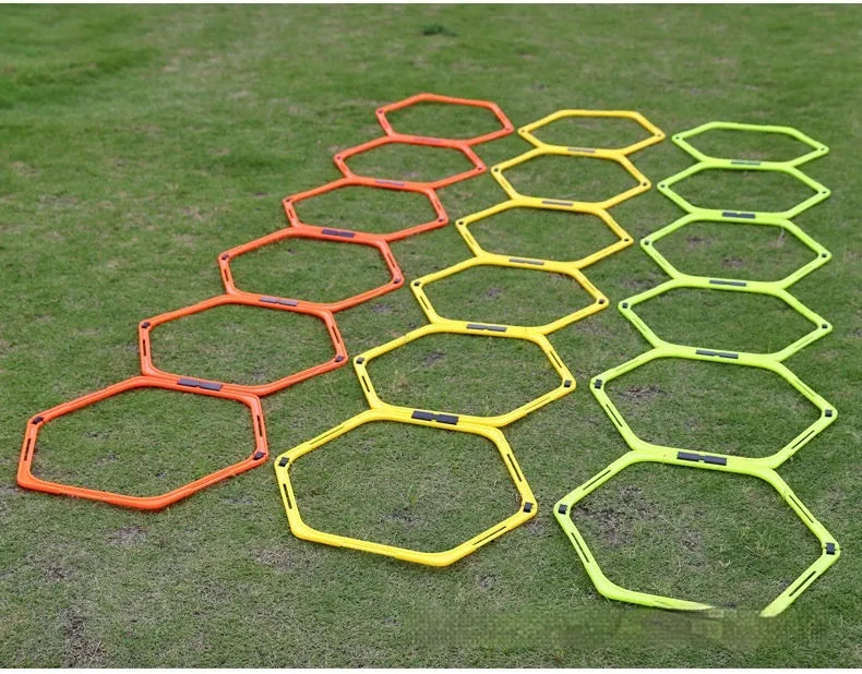 Set of six foldable yellow green and orange hexagon plastic agility training rings laid out on grass