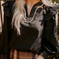 Black V-neck long sleeve blouse with ruffle detail and contrast stitching.