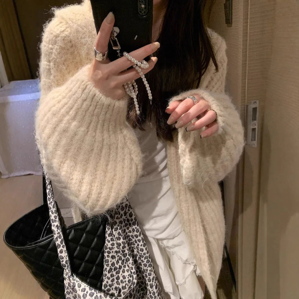 A woman's loose-fit hooded sweater cardigan in a thick fabric, shown in dark grey, brown, and milky white colour options.
