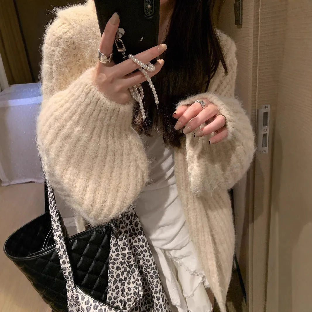 A woman's loose-fit hooded sweater cardigan in a thick fabric, shown in dark grey, brown, and milky white colour options.