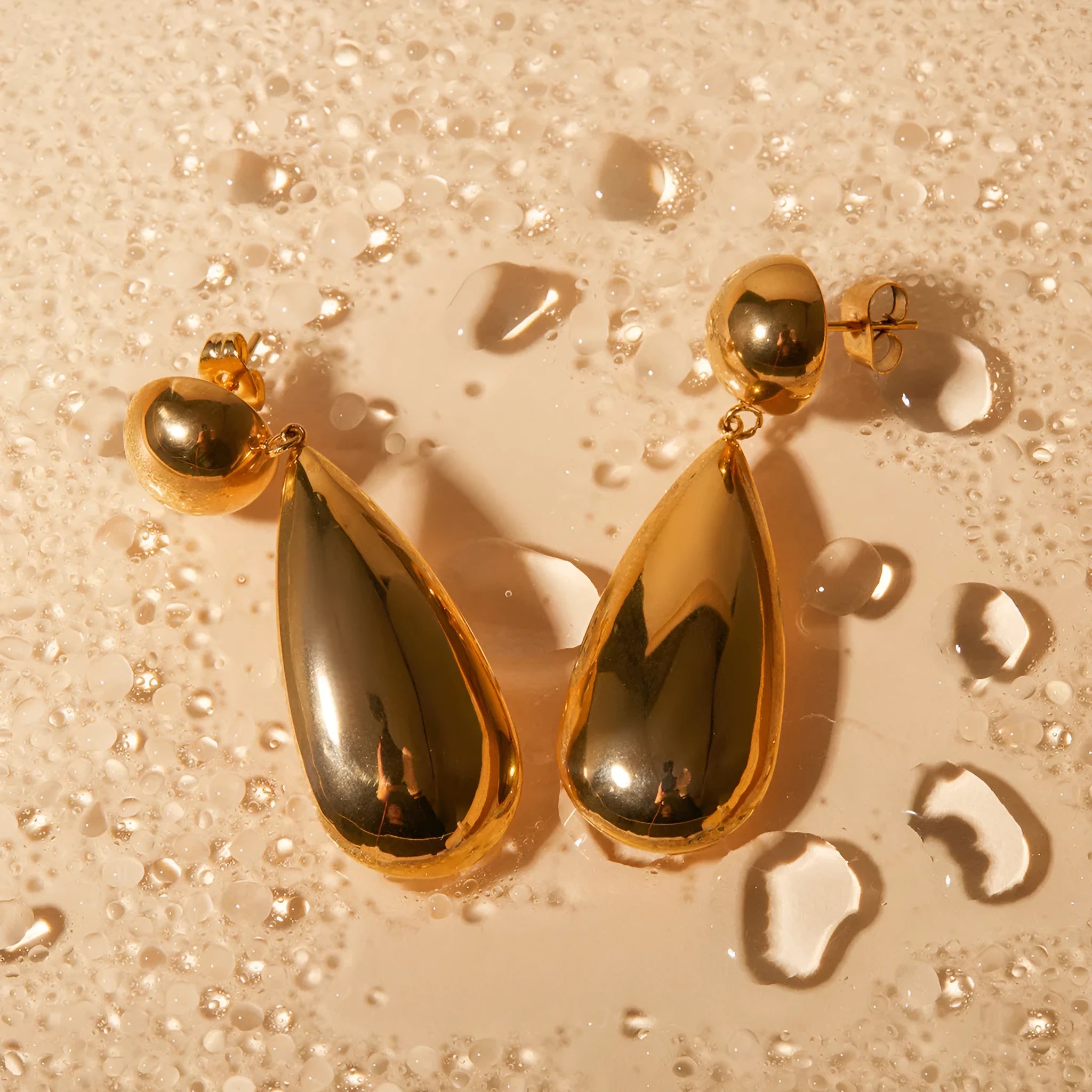 Gold stainless steel earrings with geometric hemisphere shape and water drop pendant design