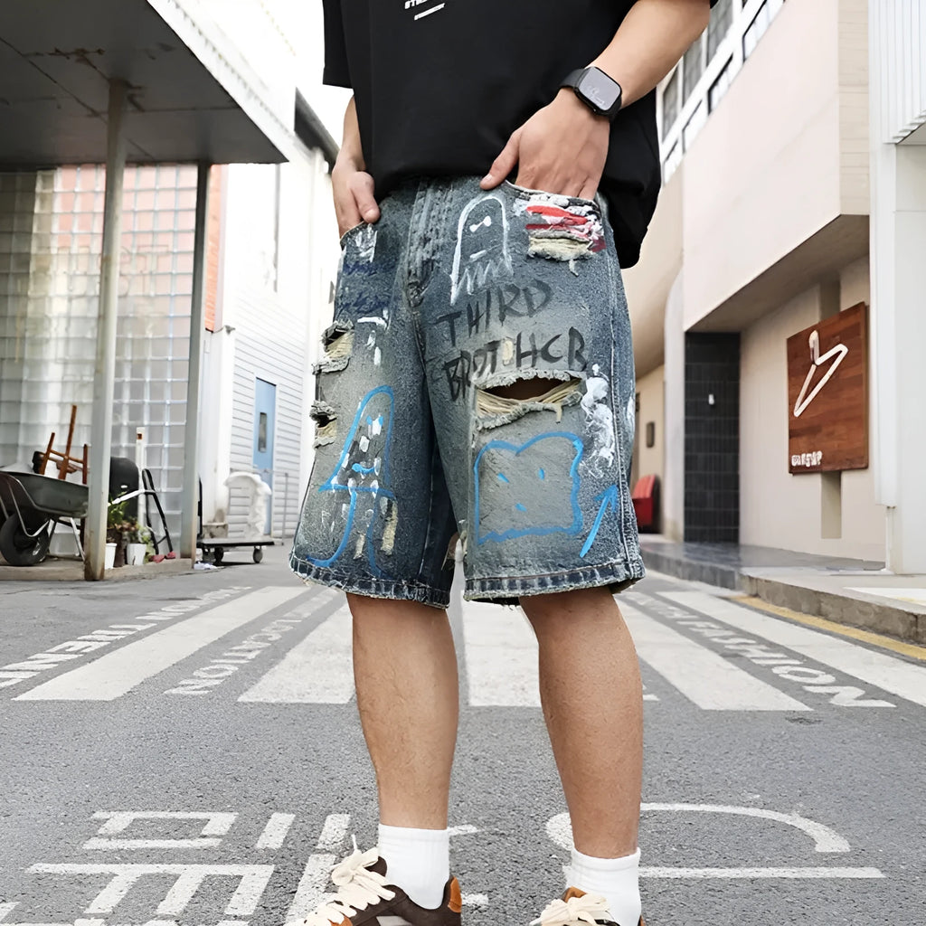 Blue distressed denim shorts with graffiti detail and ripped styling on mannequin