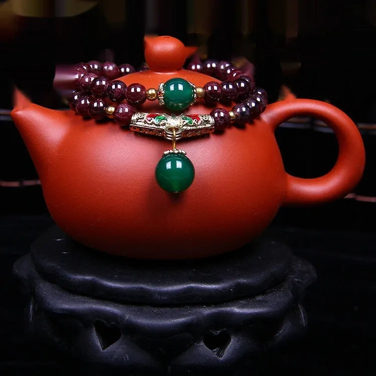 Close-up of a natural red garnet bead bracelet with a golden toad charm on a wrist.