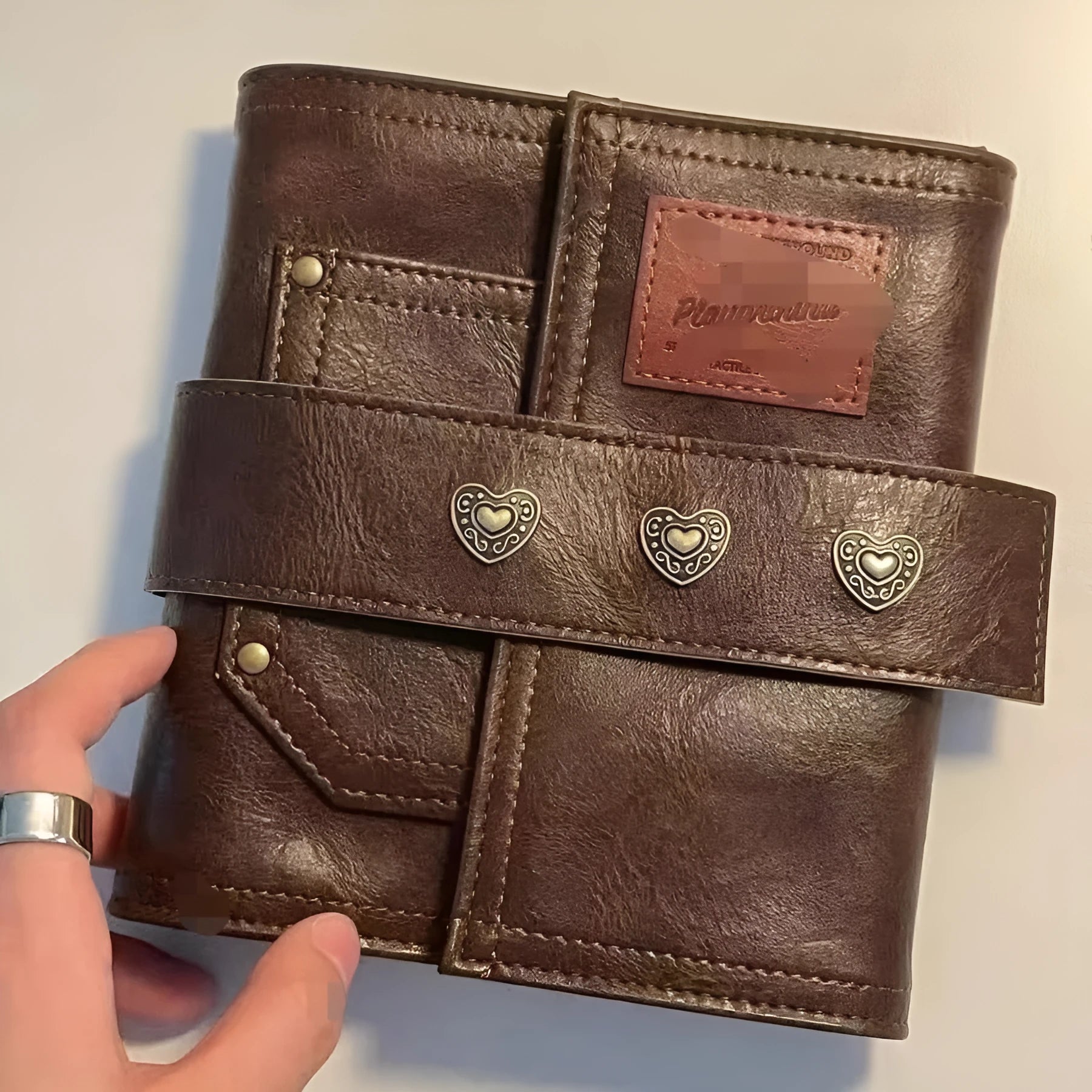 Brown retro leather-style A7 notebook with a buckle closure, shown open to reveal loose-leaf binder binding.