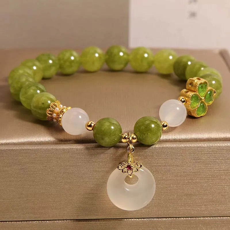 Women's green tourmaline bracelet with four-leaf clover safety buckle on a wrist.
