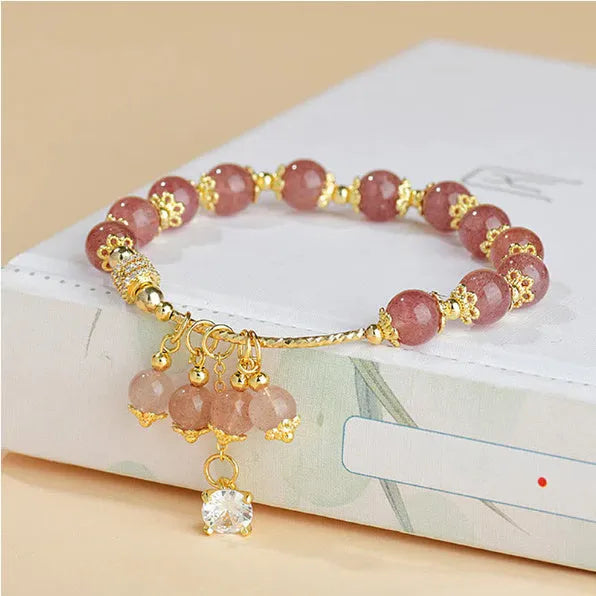 Close-up of a pink heart-shaped strawberry quartz crystal bracelet with pearl details on a wrist.
