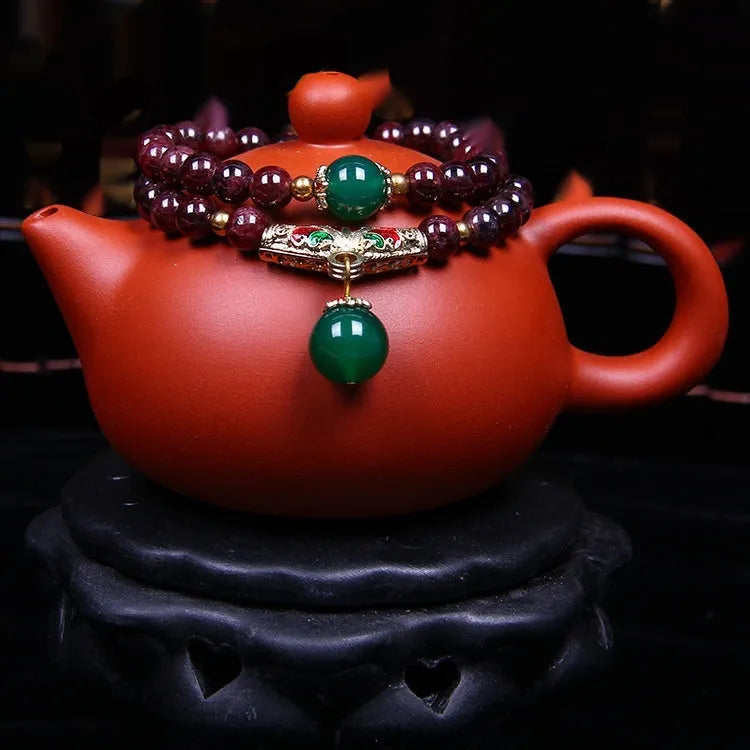 Close-up of a natural red garnet bead bracelet with a golden toad charm on a wrist.