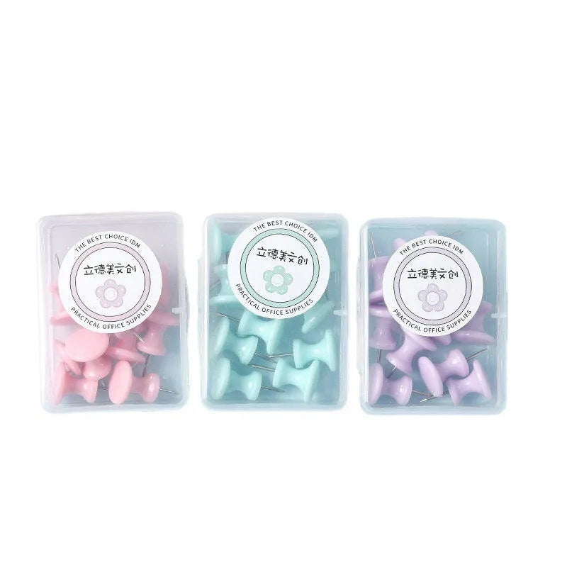 Box of coloured plastic push pins in cherry blossom pink, mint green and lavender on a white surface