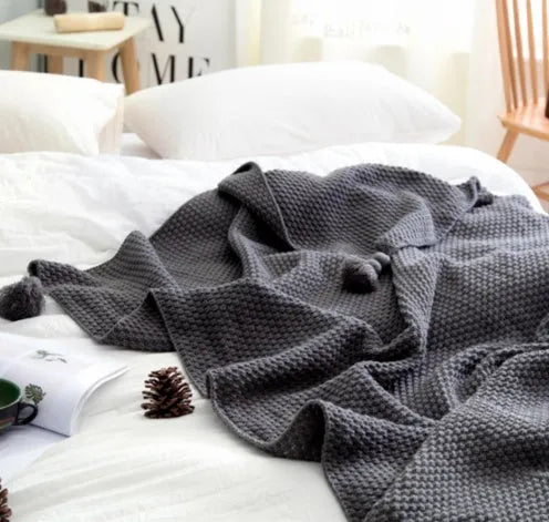 Nordic style fringed knit throw blanket in a neutral colour, shown draped over a sofa.