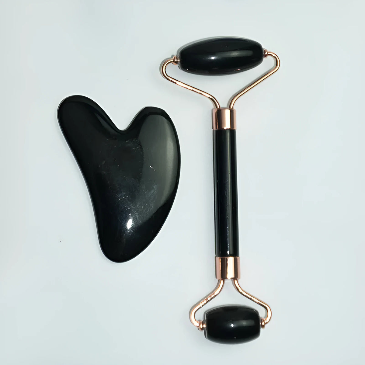 Stainless steel facial massage set showing a double-ended acupuncture pen with pointed tip and heart roller, plus a gua sha scraping plate.