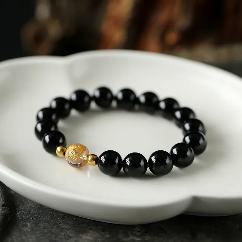 Geometric obsidian and white crystal unisex bracelet with a golden dragon bead on a wrist.
