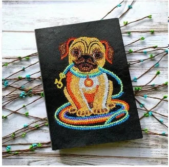Black hardcover A5 diamond painting notebook with 50 cream pages open on craft table