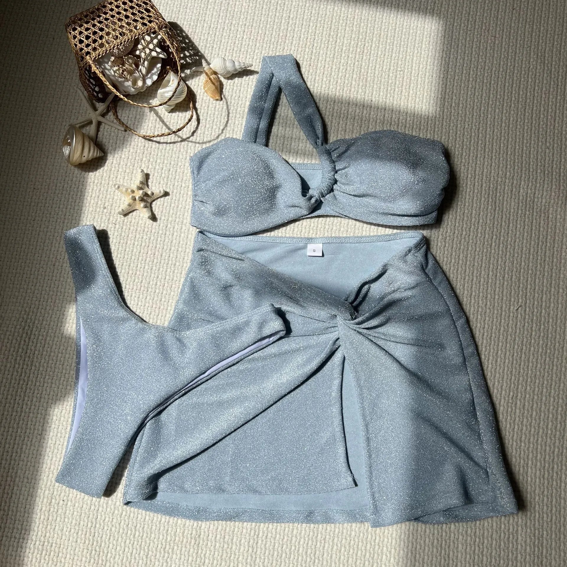 Light green one-shoulder swimsuit top, matching bikini bottoms, and cover-up skirt laid flat