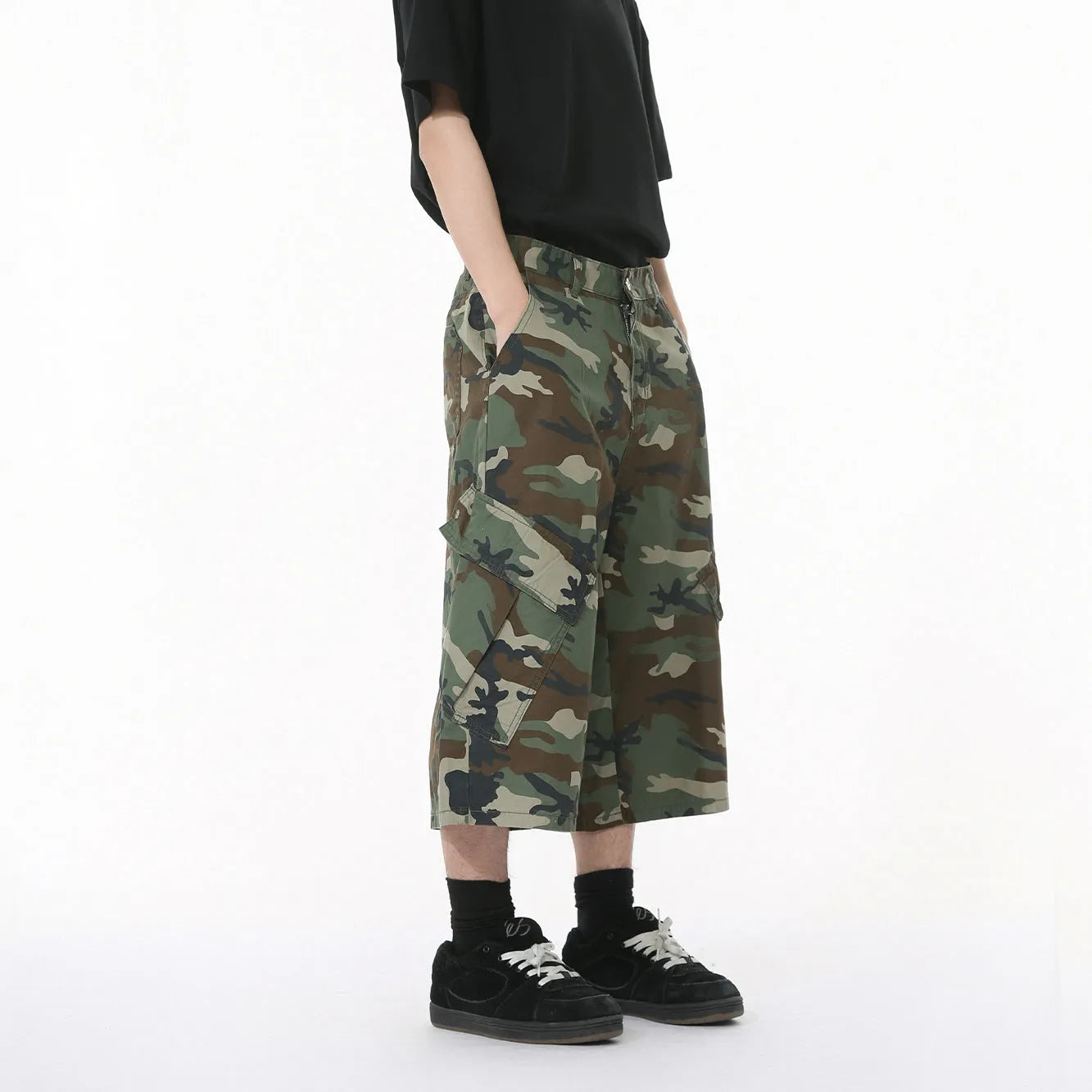 Men's loose-fit camouflage cotton trousers with wide legs, cropped hem, side stitching, and large front pockets.