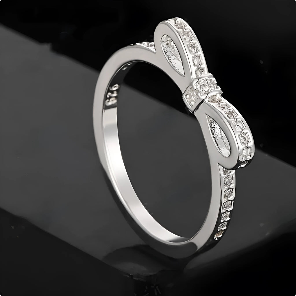 Silver-coloured bow-shaped ring with clear rhinestone embellishments on a white background