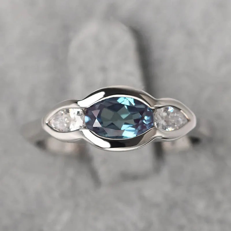 Geometric ellipse copper ring with inlaid zircon stones in white gold finish on a grey background